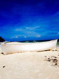 Boat moored on beach against blue sky