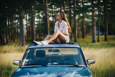 A woman sitting on the roof on a car.