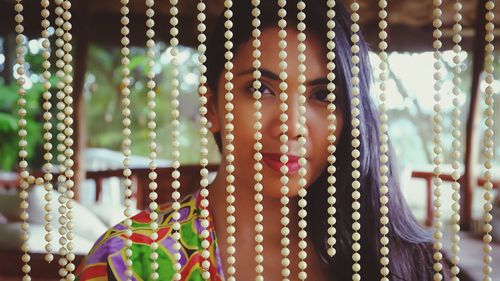 Close-up portrait of young woman seen through bead decorations