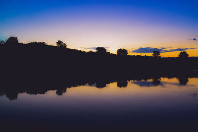 Silhouette trees by lake against sky during sunset