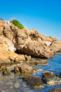 Rock formations by sea against clear blue sky