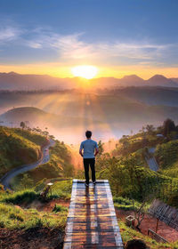 Rear view of man standing against mountains during sunset