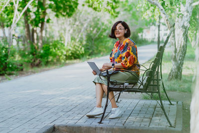 Portrait of young woman sitting on bench in park