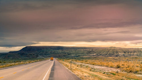 School bus on an empty road along landscape against sunset sky