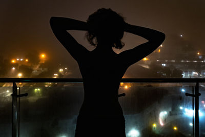 Rear view of silhouette woman standing in illuminated city against sky at night