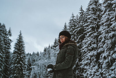 Side view portrait of young woman standing against trees during winter