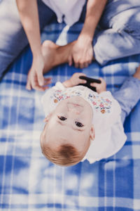 Directly above portrait of baby girl sitting by mother on picnic blanket