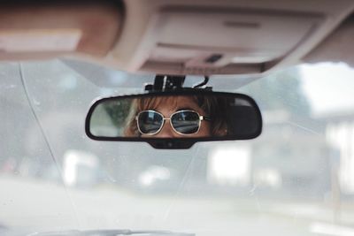 Woman wearing sunglasses reflecting on rear-view mirror in car