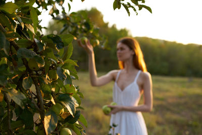 Young woman standing by tree against plants