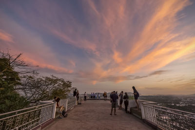 People on railing against sky during sunset