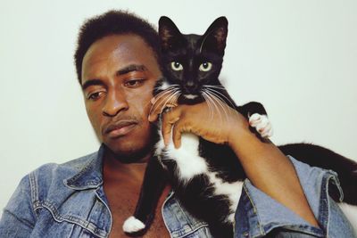 Close-up of young man with cat against white background