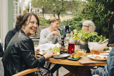 Portrait of smiling senior woman sitting with male and female friends at dining table enjoying dinner party