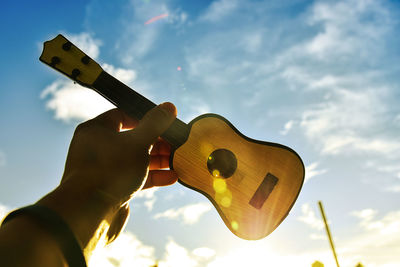 Cropped hand of person holding small guitar against sky