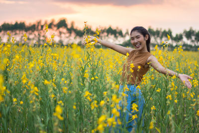 Portrait of smiling young woman standing on oilseed rape field during sunset