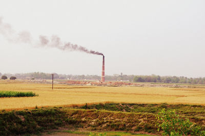 Smoke emitting from smoke stack on field against clear sky