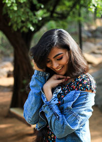 Smiling young woman wearing denim jacket standing in park