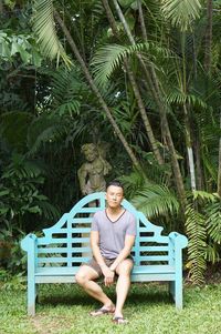 Full length portrait of man sitting on bench against trees