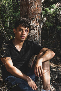 Portrait of young man sitting on tree trunk in forest