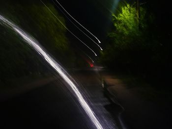 Blurred motion of light trails on road by trees at night