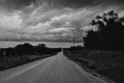 Road amidst trees on field against sky