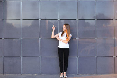 Full length of woman gesturing while standing against wall