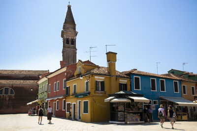 People walking by buildings in city against clear blue sky