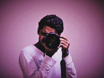 Portrait of young man photographing against wall