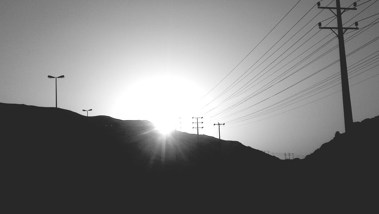 sun, sunbeam, lens flare, sunlight, silhouette, low angle view, built structure, power line, electricity pylon, clear sky, sky, architecture, building exterior, street light, bright, electricity, cable, sunset, outdoors, sunny