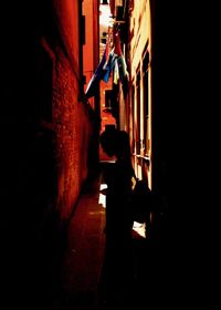 Rear view of woman walking in alley amidst buildings at night