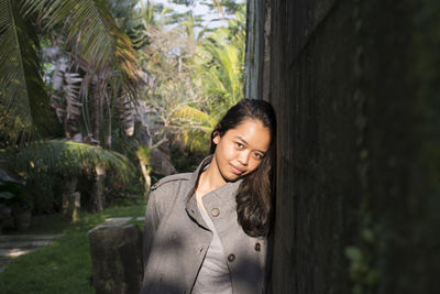 Smiling young woman standing by tree trunk