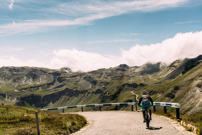 Woman riding bicycle on mountain road against sky