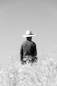 Rear view of woman wearing hat standing on field against clear sky