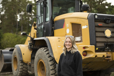 Smiling young woman standing next to excavator