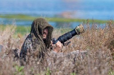 Portrait of man photographing on land against lake