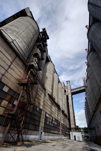 Low angle view of silos against cloudy sky