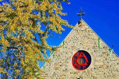 Low angle view of cross by building against clear blue sky
