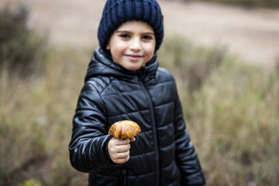 Portrait of smiling boy holding mushroom while standing on land