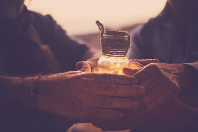 Cropped image of friends holding illuminated jar during sunset