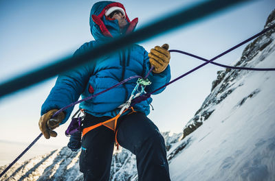 Male climber belays his lead climber during a cold winter alpine climb