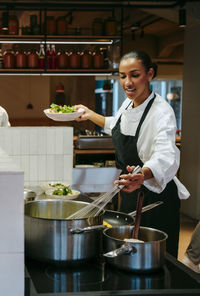 Female chef stirring with wire whisk while holding salad bowl in commercial kitchen
