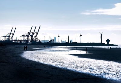 Silhouette cranes on pier by sea against sky