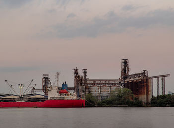 Cranes at commercial dock against sky during sunset