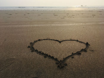 Heart shape on sand at beach against sky