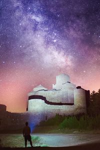 Rear view of man standing by building against sky at night