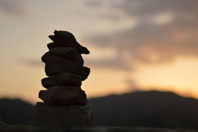 Stack of stones on rock against sky during sunset