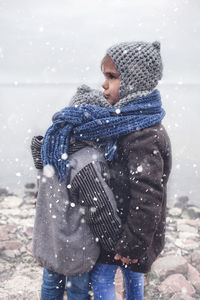 Cute smiling siblings embracing by lake during winter