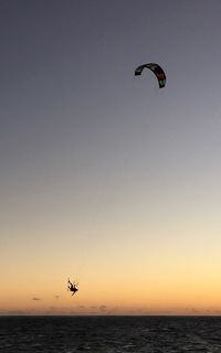 Silhouette paragliding over sea against sky during sunset