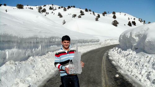 Portrait of man holding ice while standing on road against snowcapped mountain