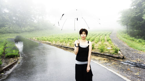 Woman holding umbrella while standing on wet road