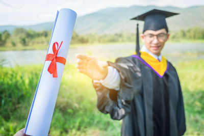 Man in graduation gown reaching diploma against sky